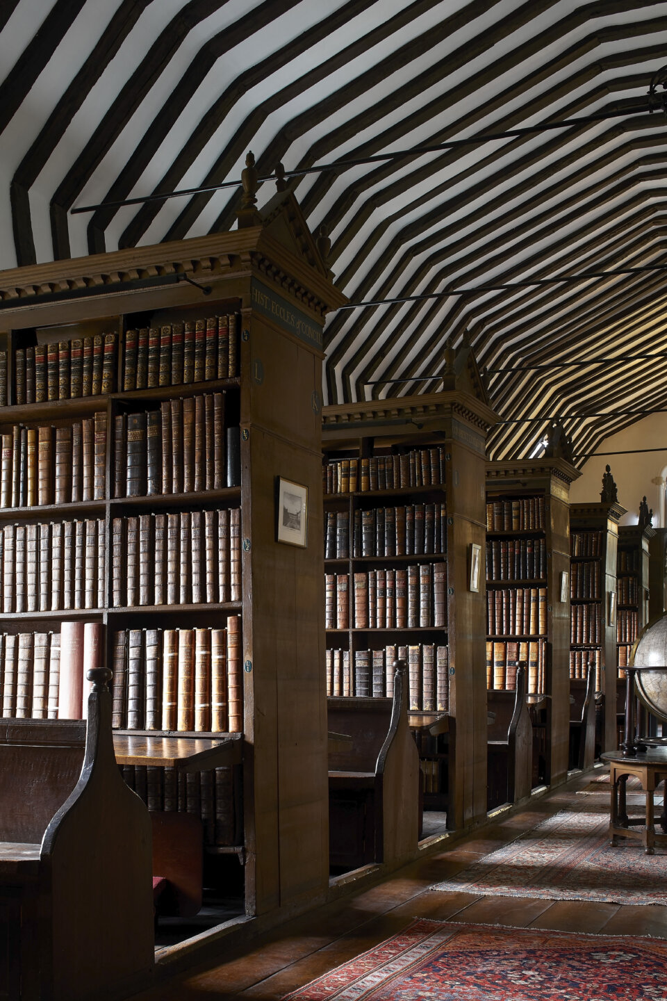 Wooden bookshelves with books and historic globes in a 16th century library