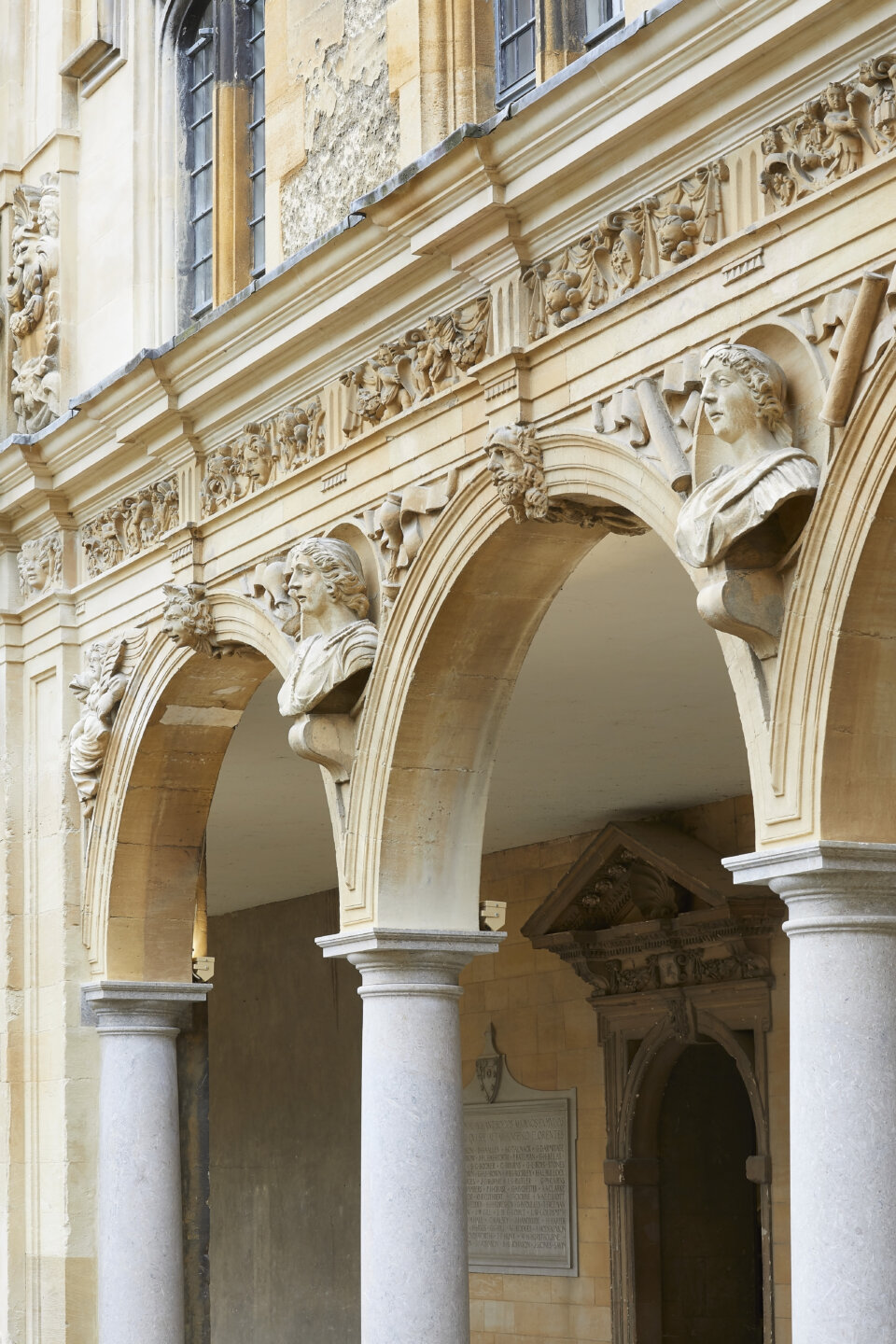 Carved decorative frieze with stone heads above columns and arched colonnade