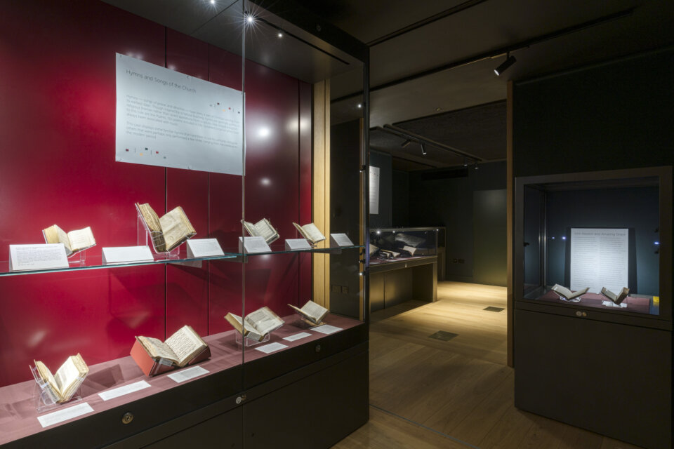 Low lit gallery space with glass display case of books.