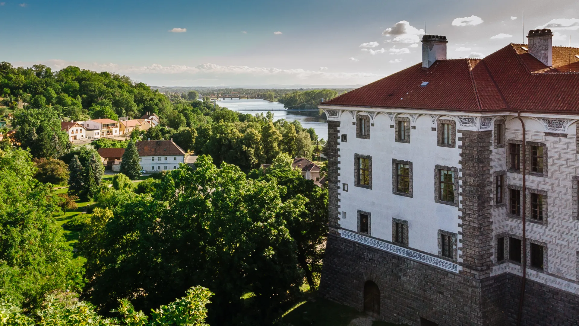 Aerial view of Nelahozeves Castle in a wooded landscape by a river with smaller buildings in the distance