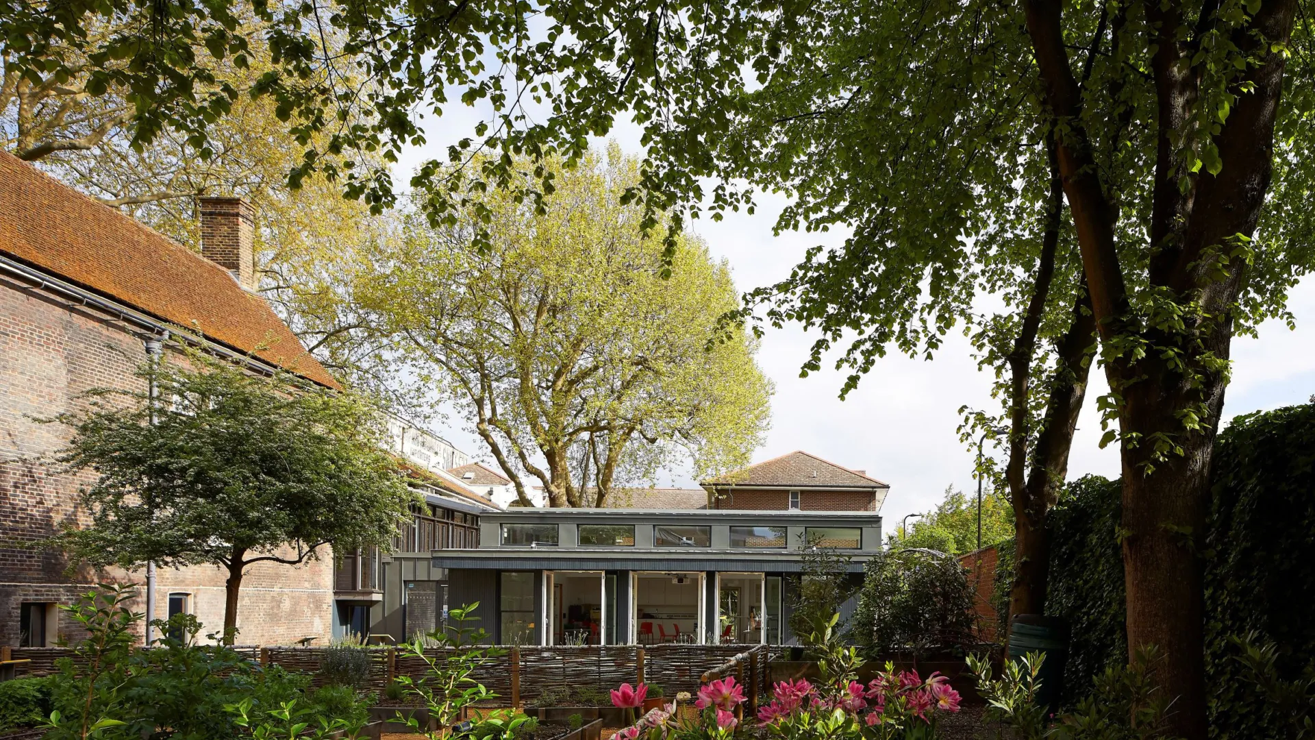 Exterior image of the Museum of the Home with two buildings set within a landscaped courtyard full of flowers and trees.