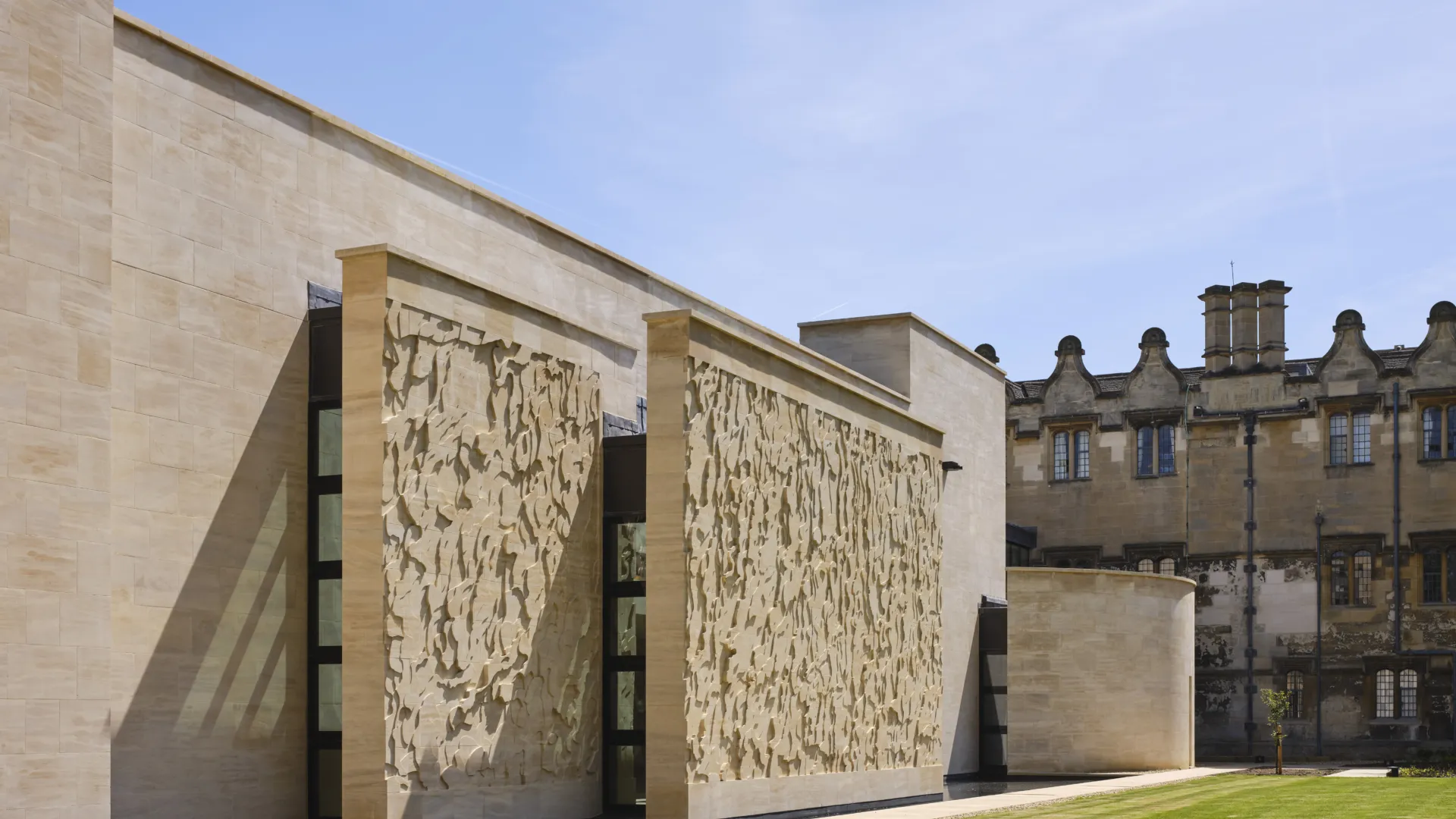 Exterior facade of a contemporary stone building with a small reflecting pool and large lawn in front of it.