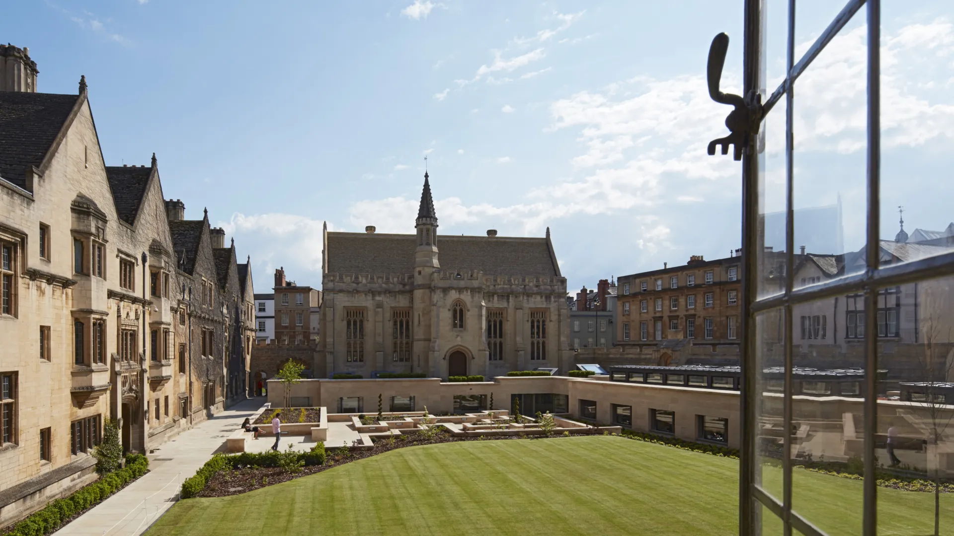 View from an open window across a green lawn to a sunken courtyard and historic building at Magdalen College Oxford