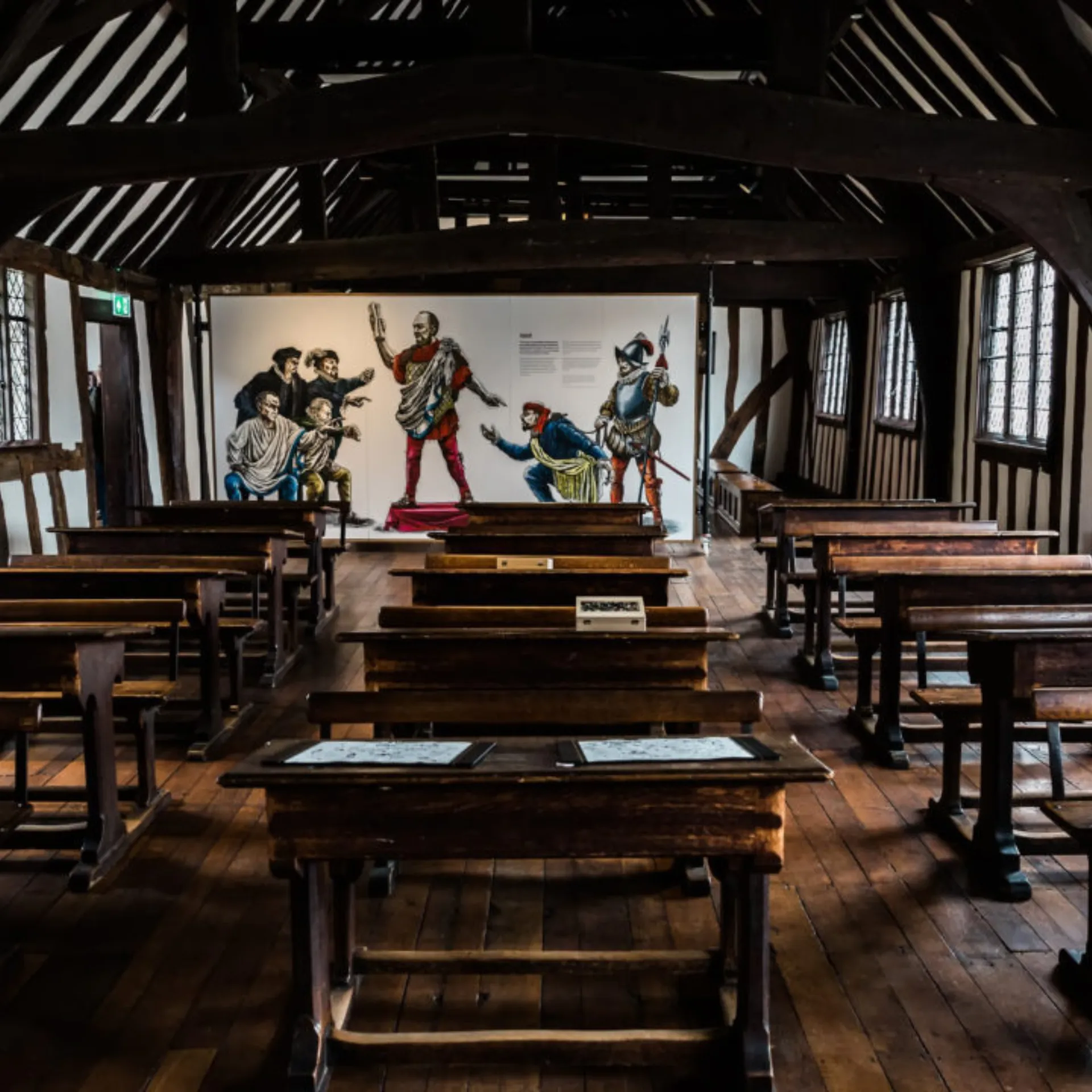 Interior of Shakespeare's school in Stratford-Upon-Avon with several benches and desks under a wooden beamed ceiling.