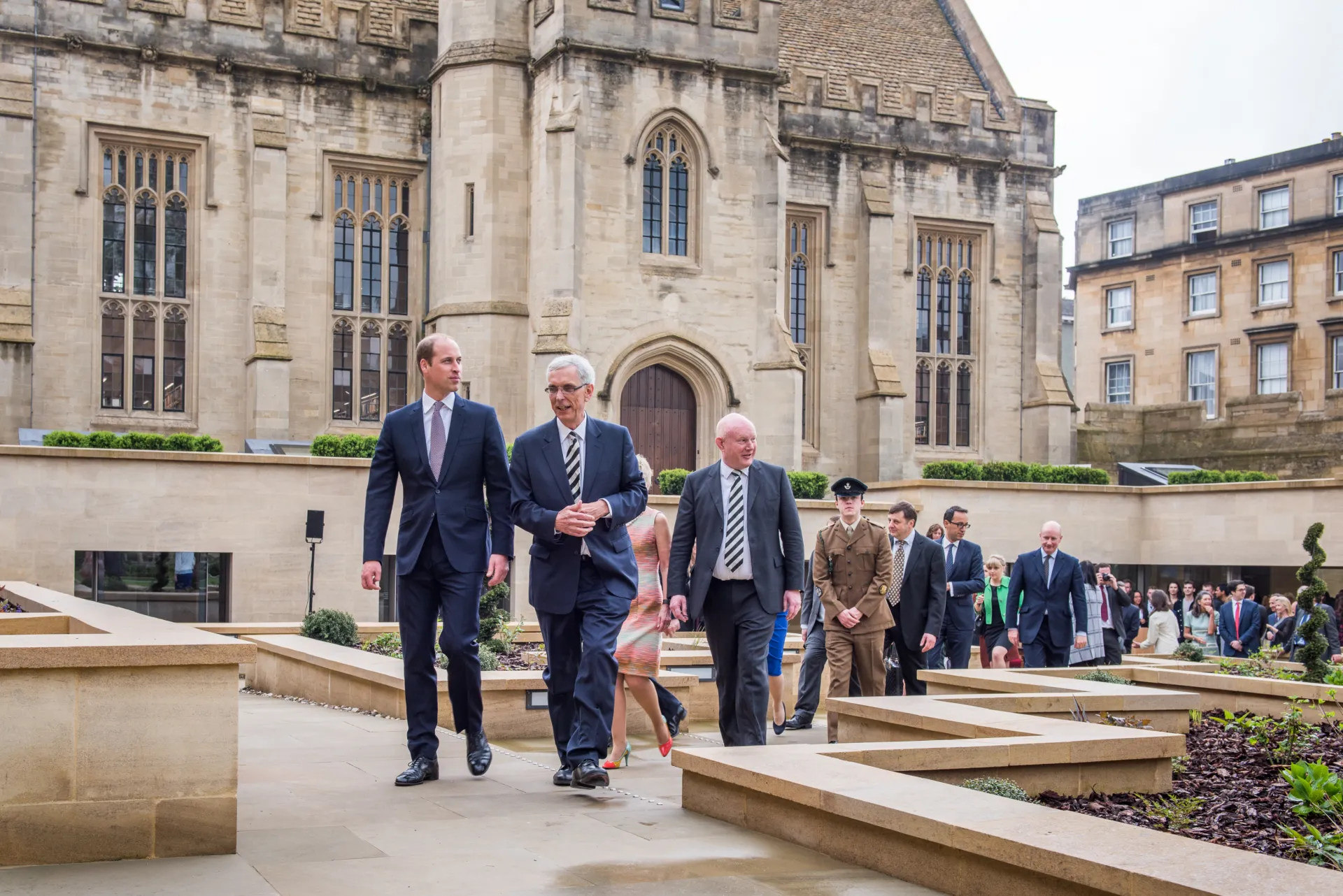 Several individuals in suits walk across the courtyard of Magdalen College in Oxford led by Prince William, Duke of Cambridge.