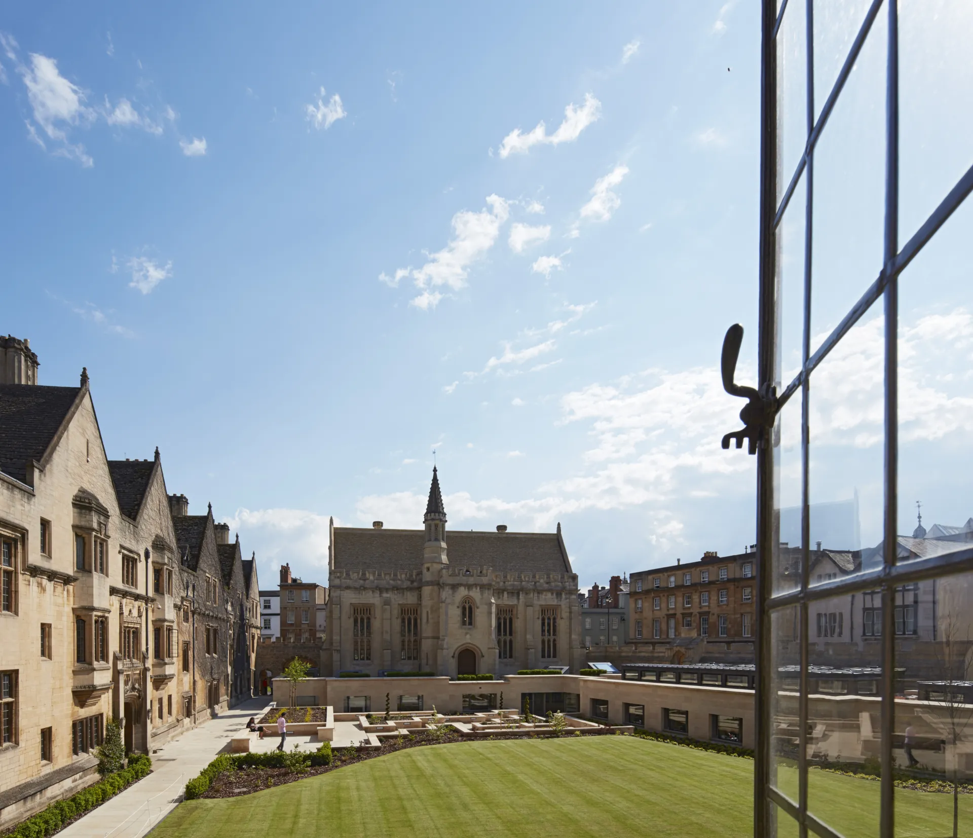 View from an open window across a green lawn to a sunken courtyard and historic building at Magdalen College Oxford