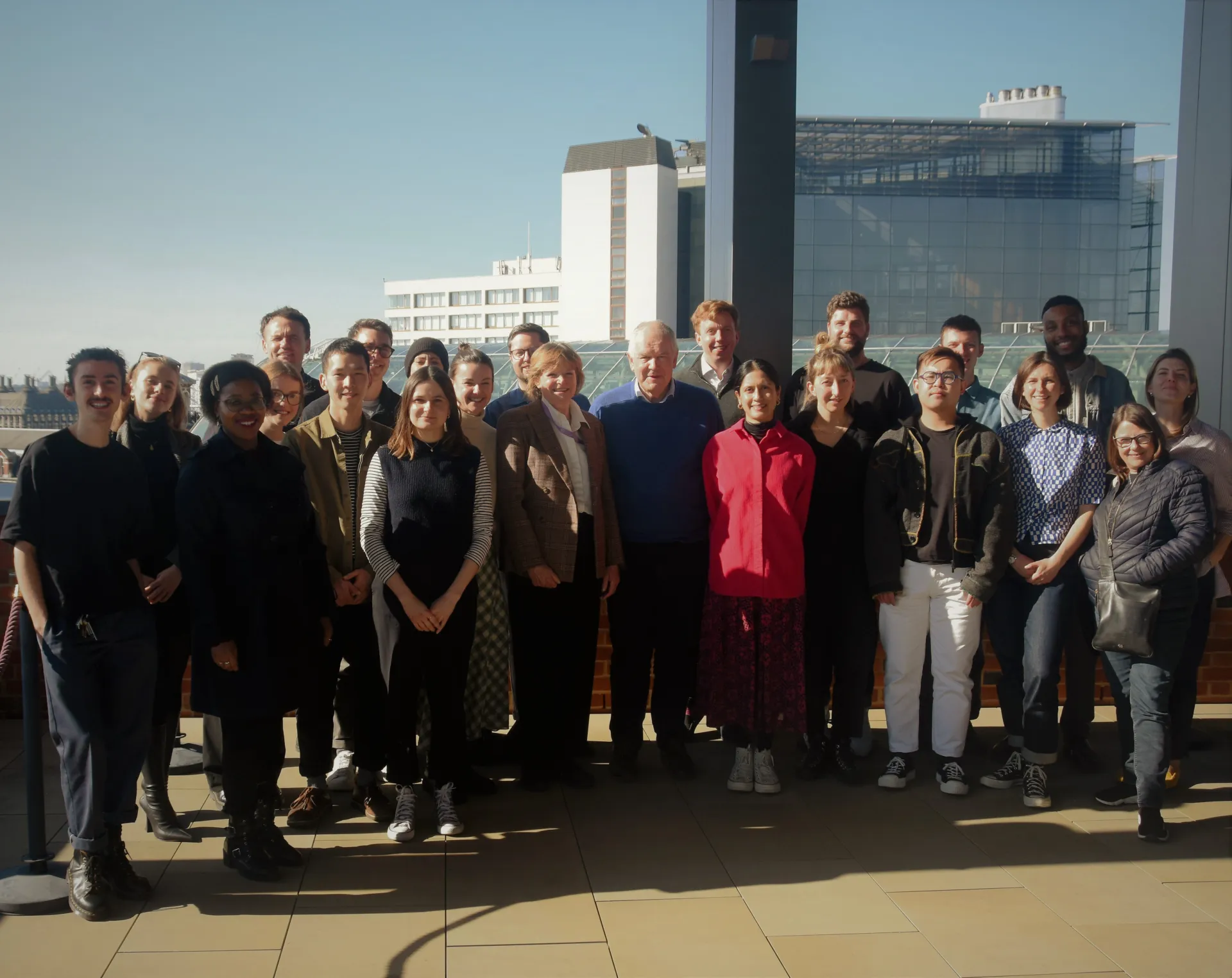 Group of approximately 30 people standing on a terrace overlooking London skyline.
