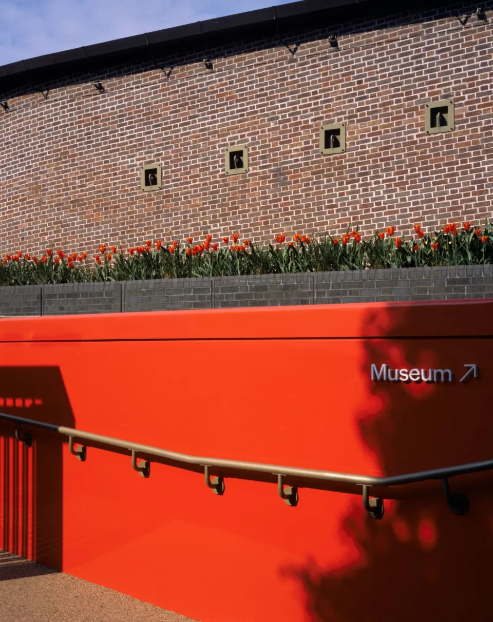 Entrance to the Museum of the Home with a red entrance ramp and brick wall with red tulips in the background