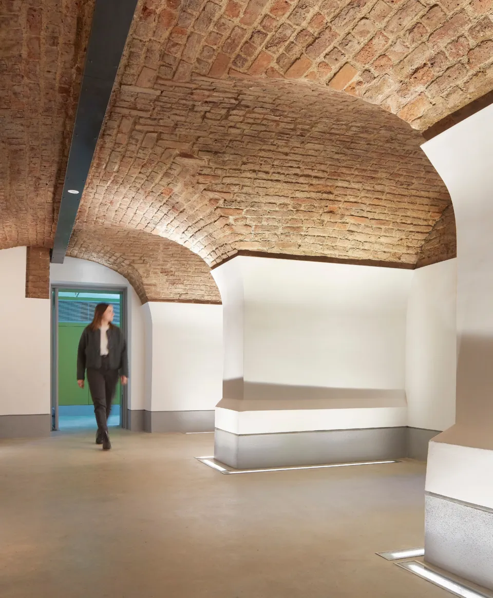 a woman walks into a vaulted exhibition gallery in the museum of the home with brick ceilings and white walls