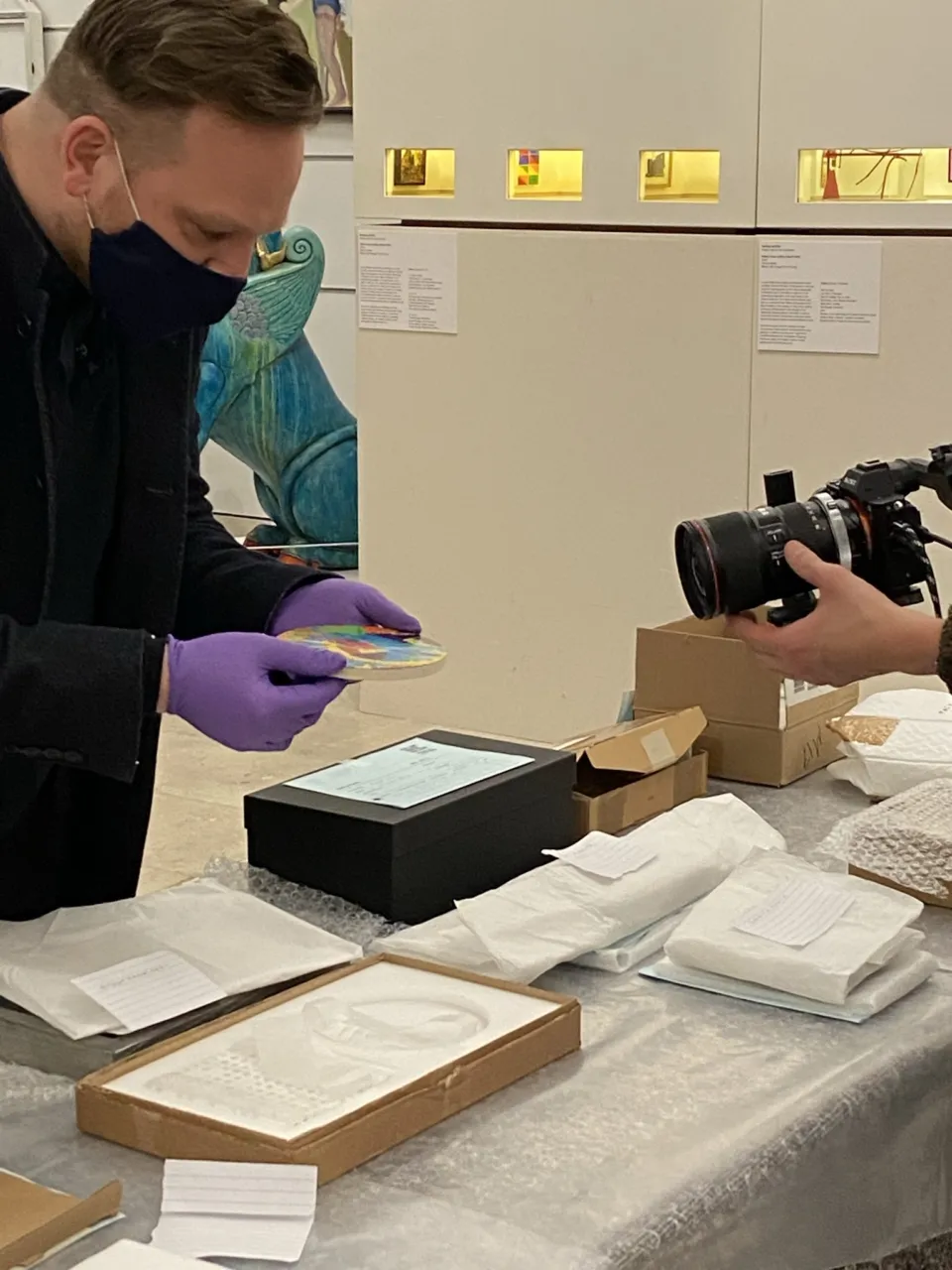Man wearing mask looks at miniature pieces of art work