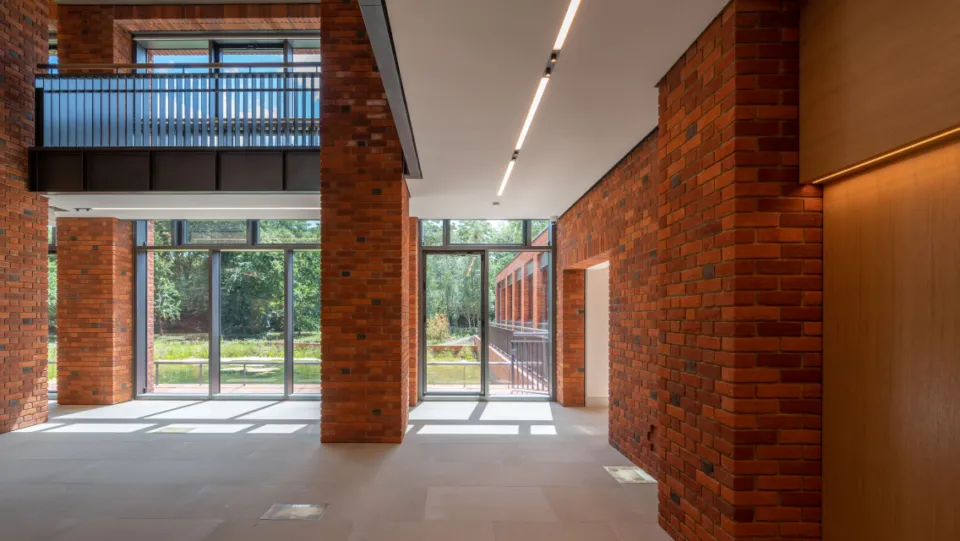 Sunlit interior of the foyer of Lambeth Palace Library. Brick walls and glass windows with views of the garden beyond.