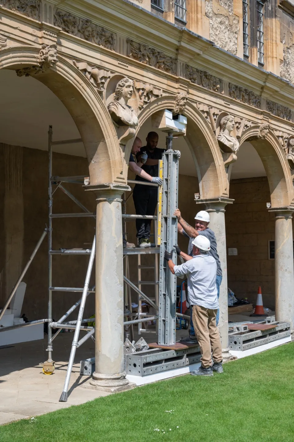 Three men install stone columns beneath a historic archway on a stone building.