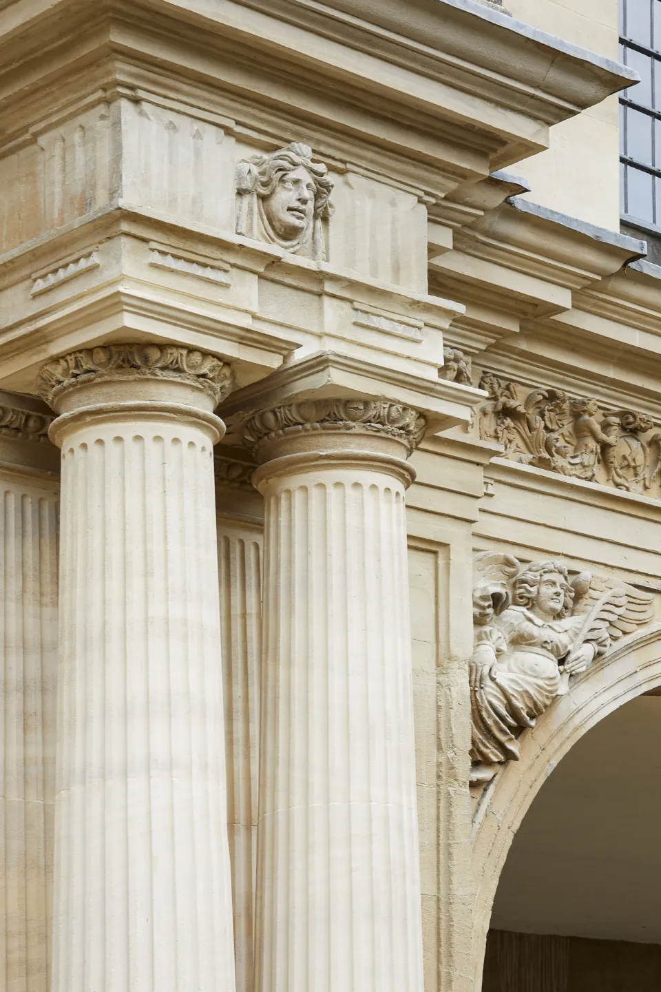 Fluted stone column beneath a decorative stone frieze with carved heads and angels