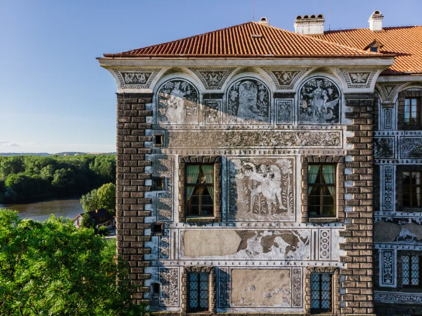 An image of a decorated facade of the Nelahozeves Castle set within a forested landscape in the Czech Republic