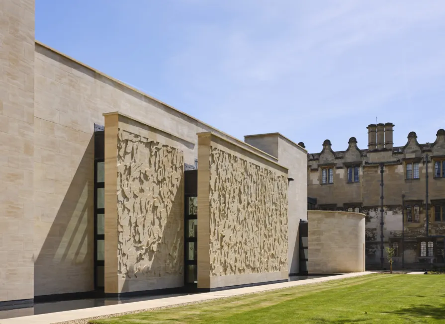 Exterior facade of a contemporary stone building with a small reflecting pool and large lawn in front of it.