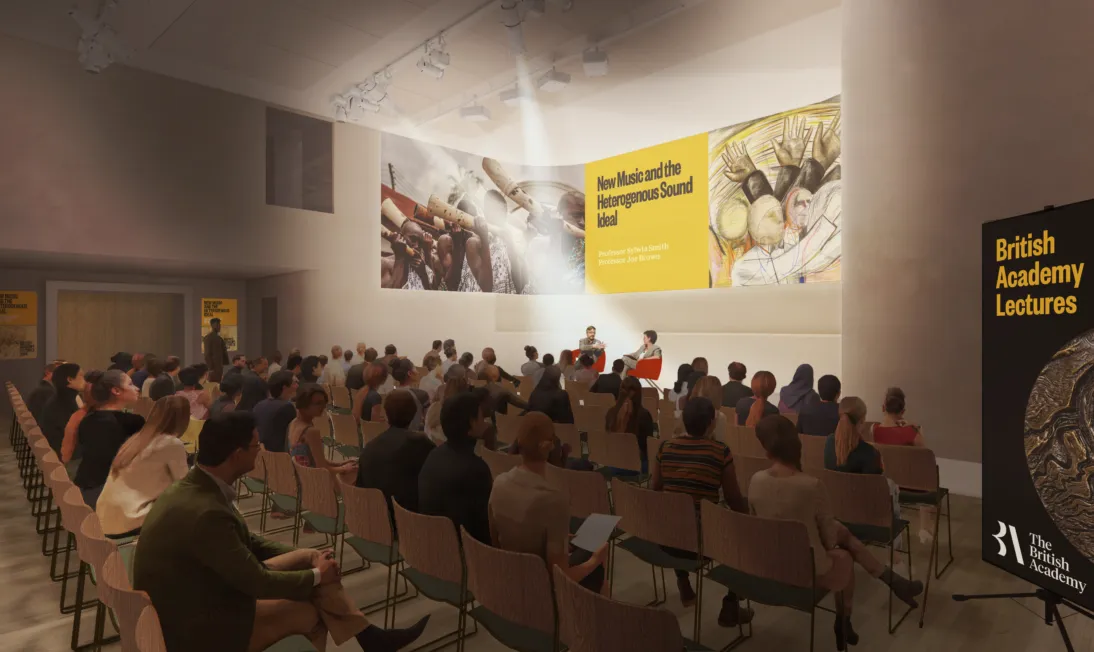 Large group of people sat in rows in a room, watching two speakers on a stage.