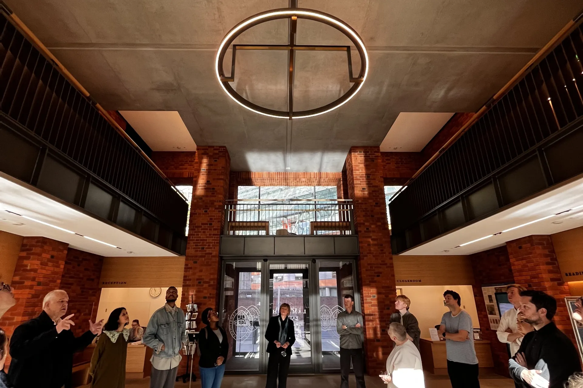 Members of Wright and Wright Architects stand in a circle in the foyer of Lambeth Palace Library listening to Clare Wright speak.