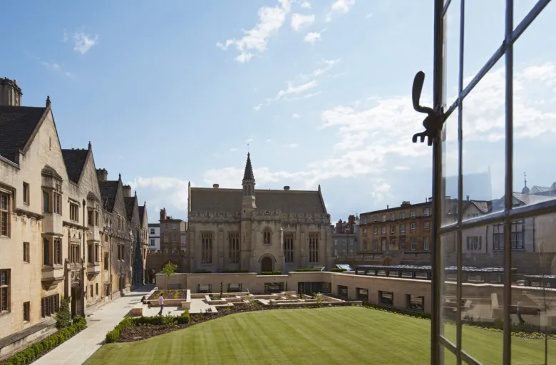 View from an open window across a green lawn to a sunken courtyard and historic building at Magdalen College Oxford