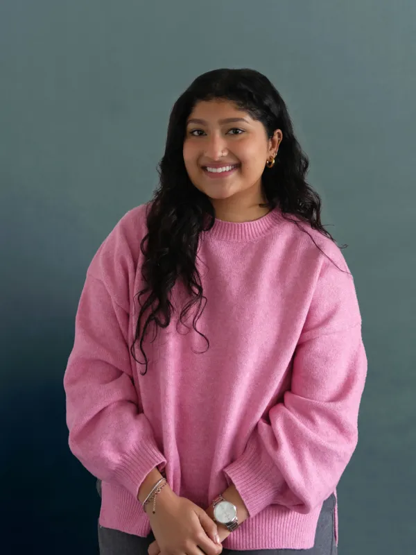 Portrait image of a woman wearing a pink jumper and with black hair