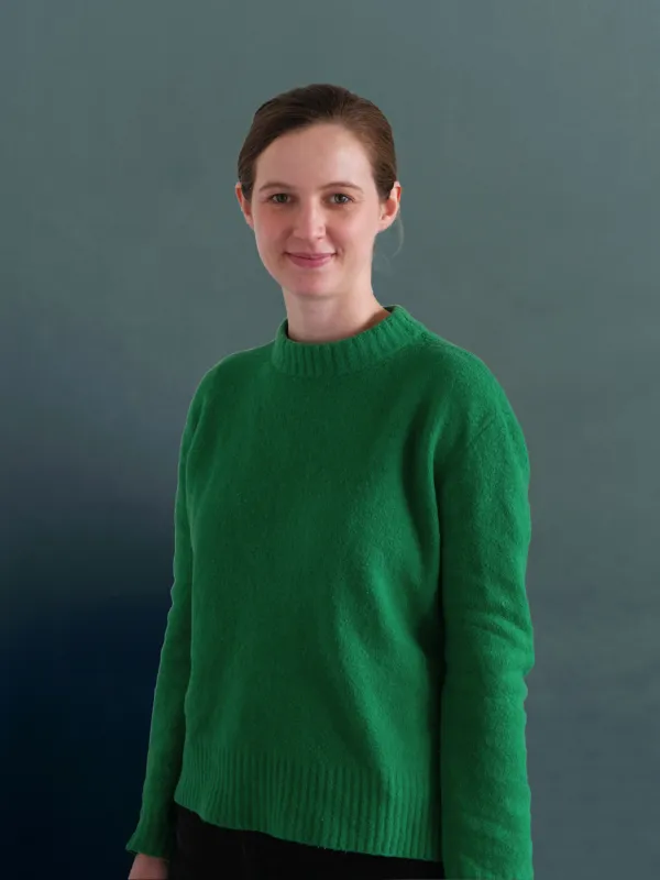 Portrait image of a woman wearing a green jumper and with brown hair tied back