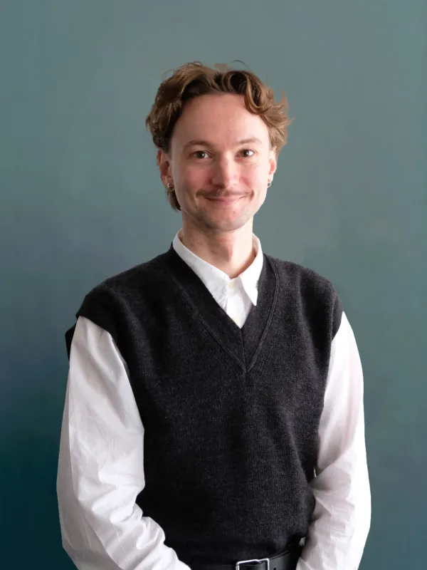 Portrait image of a man wearing a vest and a white shirt underneath with brown hair